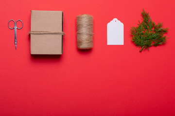 Composition of scissors, box, rope, card and tree branches on red background