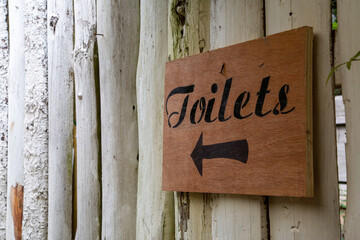 a rustic wooden sign on a wall pointing to toilets