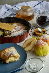 A piece of pear pie for tea on a blue plate on a white table with pears in the foreground