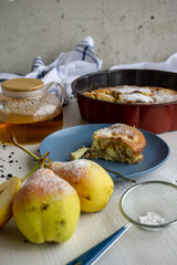 A piece of pear pie for tea on a blue plate on a white table with pears in the foreground