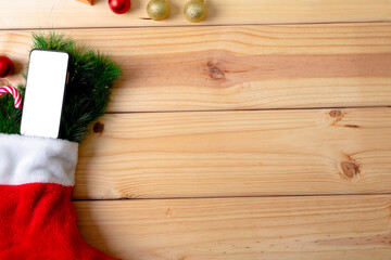 Composition of christmas stocking with fir tree, smartphone and copy space on wooden background