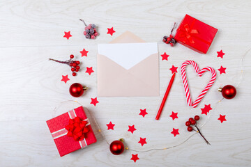 Composition of christmas decorations with envelope, baubles, candy canes, stars on wooden background