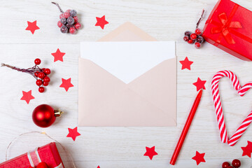 Composition of christmas decorations with envelope and red stars on white wooden background
