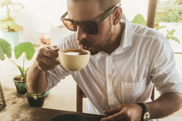 Mężczyzna pijący kawę w kawiarni w słoneczny dzień. - obrazy, fototapety, plakaty