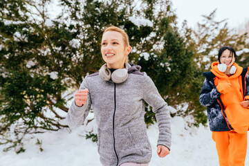 Running women in snowy winter park. Winter running exercise. Runner jogging in snow. Two middle age good looking women fitness models running in a city park outdoor.