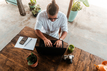 Mężczyzna, cyfrowy nomada pracujący z laptopem i telefonem przy stoliku w kawiarni, praca zdalna podczas podróży. - obrazy, fototapety, plakaty