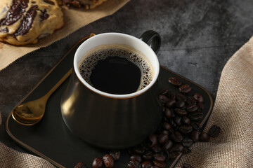 Close up Hot fresh black coffee in a luxury black cup with foam and coffee beans on black table background. Drink concept.