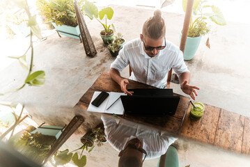 Mężczyzna pracujący przy laptopie z telefonem, praca zdalna podczas podróży, cyfrowy nomada w kawiarni.