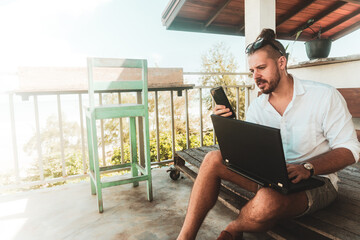 Mężczyzna, cyfrowy nomada pracujący z laptopem i rozmawiający przez telefon komórkowy w słoneczny dzień.