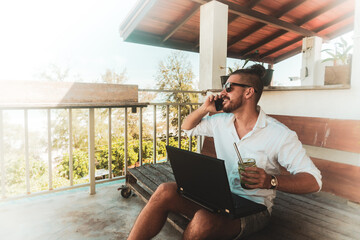 Mężczyzna, cyfrowy nomada pracujący z laptopem i rozmawiający przez telefon komórkowy w słoneczny dzień. - obrazy, fototapety, plakaty