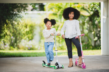 Two playful African sisters with curly hair enjoying and playing while riding scooter on empty lane...