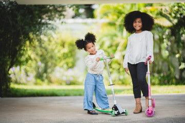 Two playful African sisters with curly hair enjoying and playing while riding scooter on empty lane...