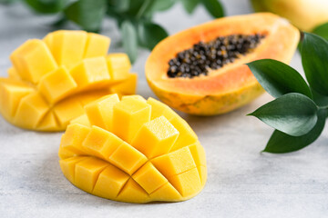 Sweet ripe mango and papaya tropical fruit cut in half on grey concrete background closeup view