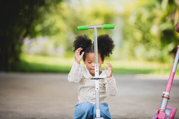 Two playful African sisters with curly hair enjoying and playing while riding scooter on empty lane...