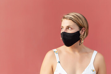 Young blonde woman with black mask looking sideways on a red background