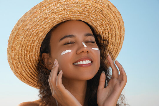 Beautiful African American woman with sun protection cream on face against blue sky