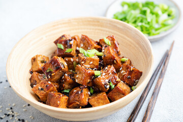 Fried tofu cubes with sauce and sesame seeds in a bamboo bowl, closeup view