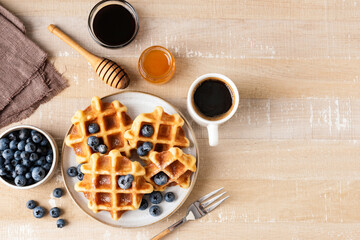 Sweet belgian waffles with blueberries, honey and cup of black coffee on a wooden table background,...