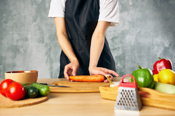 Woman in a black apron in the kitchen cutting vegetables cooking salad vitamins