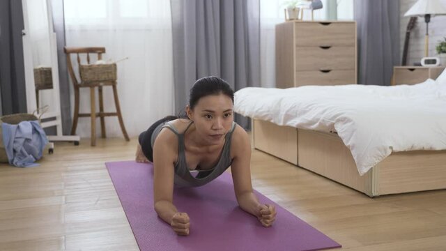 fit asian woman is holding the plank position on an exercise mat in the morning at background modern bright home interior.
