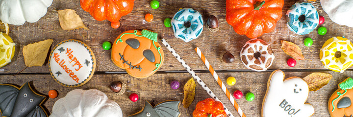 Halloween cookies, sweets and decor background. Trick or treat concept. Traditional halloween gingerbread, candy with pumpkins and decorations on wooden background top view copy space