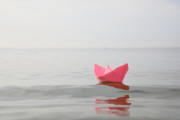 Pink paper boat on water surface, space for text