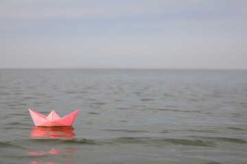 Pink paper boat on water surface, space for text