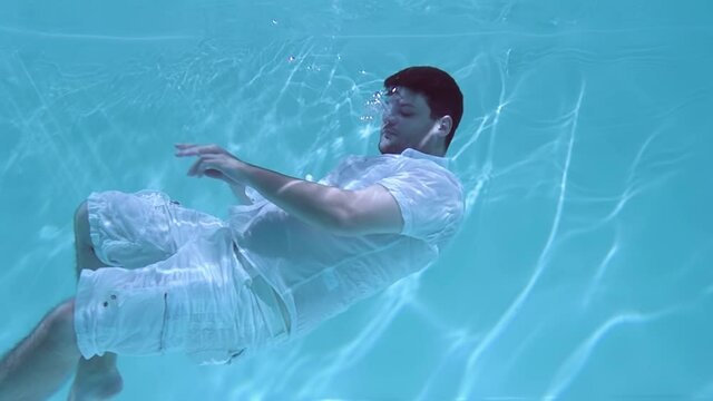 Man in clothes wallows underwater. He sinks into the water.