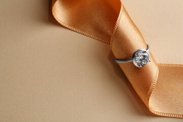Beautiful luxury engagement ring with gemstone and ribbon on beige background, closeup. Space for...