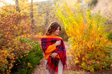 a young woman in an orange sweater wraps herself in a scarf in an autumn park