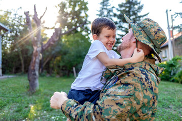 Cropped shot of a young soldier men and son in a park. Military man father hugs son. Cute Caucasian boy hugs his dad in the front yard. His dad has return from overseas military assignment.