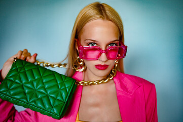 Confident woman with trendy green quilted leather bag on her neck. Model wearing pink sunglasses, big earrings. Fashion accessories advertising concept. Close up portrait. Copy, empty space for text