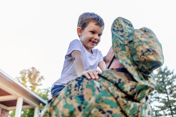 Cropped shot of a young soldier men and son in a park. Military man father hugs son. Cute Caucasian boy hugs his dad in the front yard. His dad has return from overseas military assignment.