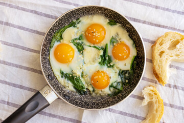 Top views to fried eggs with spinach, cheese and hemp seeds in skillet. Healthy breakfast or brunch.