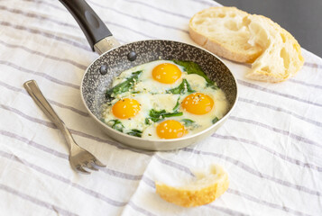 Selective focus to fried eggs with spinach, cheese and hemp seeds in skillet. Healthy breakfast or brunch.