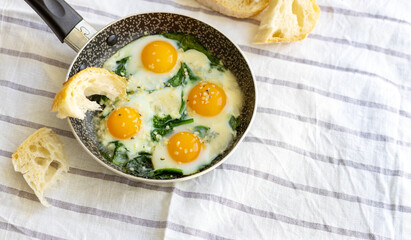 Selective focus to fried eggs with spinach, cheese and hemp seeds in skillet. Healthy breakfast or brunch.
