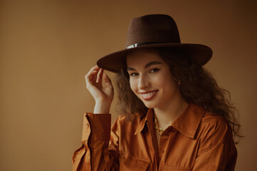 Happy smiling brunette woman wearing trendy brown hat, shirt dress, posing in studio. Copy, empty space for text