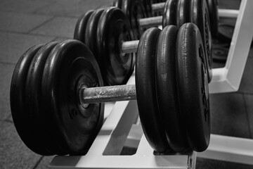 Heavy dumbbells in the gym. sports dumbbells in in a rack in sports club. black and white photo .