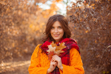 a young woman in an orange sweater wraps herself in a scarf in an autumn park