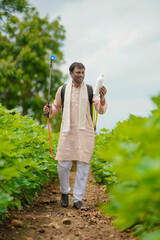Young indian farmer showing liquid fertilizer bottle at agriculture field.