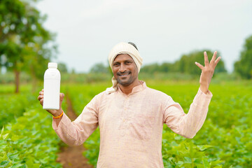 Young indian farmer showing liquid fertilizer bottle at agriculture field.