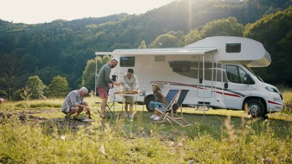 Multi-generation family preparing dinner outdoors by car, caravan holiday trip. - Powered by Adobe