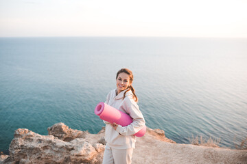 Smiling cheerful woman 25-26 year old hold yoga mat wear training hoodie posing over sea nature...