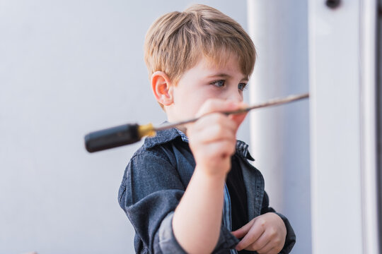 Attentive boy with manual screwdriver against window