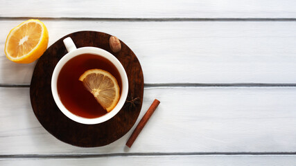 A cup of tea with lemon, honey and cinnamon sticks, star anise on a white wood background. Christmas, winter concept