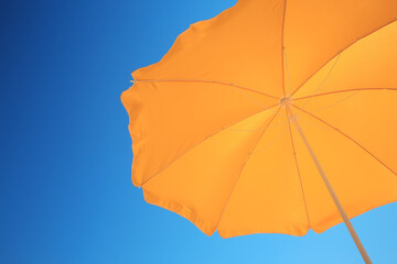 Orange beach umbrella against blue sky, space for text