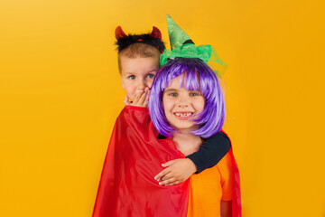 One little toddler boy and girl in a carnival costume for Halloween is isolated on a yellow background. Traditions, holidays concept.