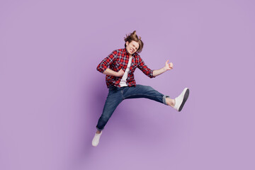 Portrait of entertainer careless cheerful guy jump play imaginary instrument on purple background
