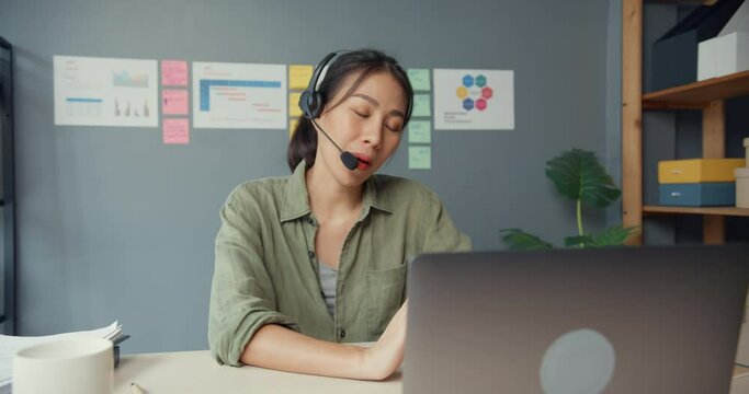 Asia businesswoman using laptop talk to colleagues about plan in video call while work from house at living room. Customer service agents or call center, social distancing, quarantine for coronavirus.
