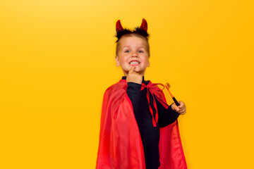 One little toddler boy in a carnival costume with toothpaste and an orange brush for Halloween is isolated on a yellow background. Medicine, dental hygiene, holidays concept.